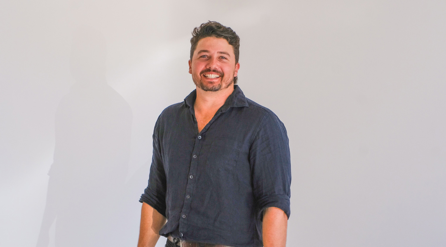 Jack Carew from Growth Huntr is standing in a dark blue, collared, button-up shirt in front of a white background