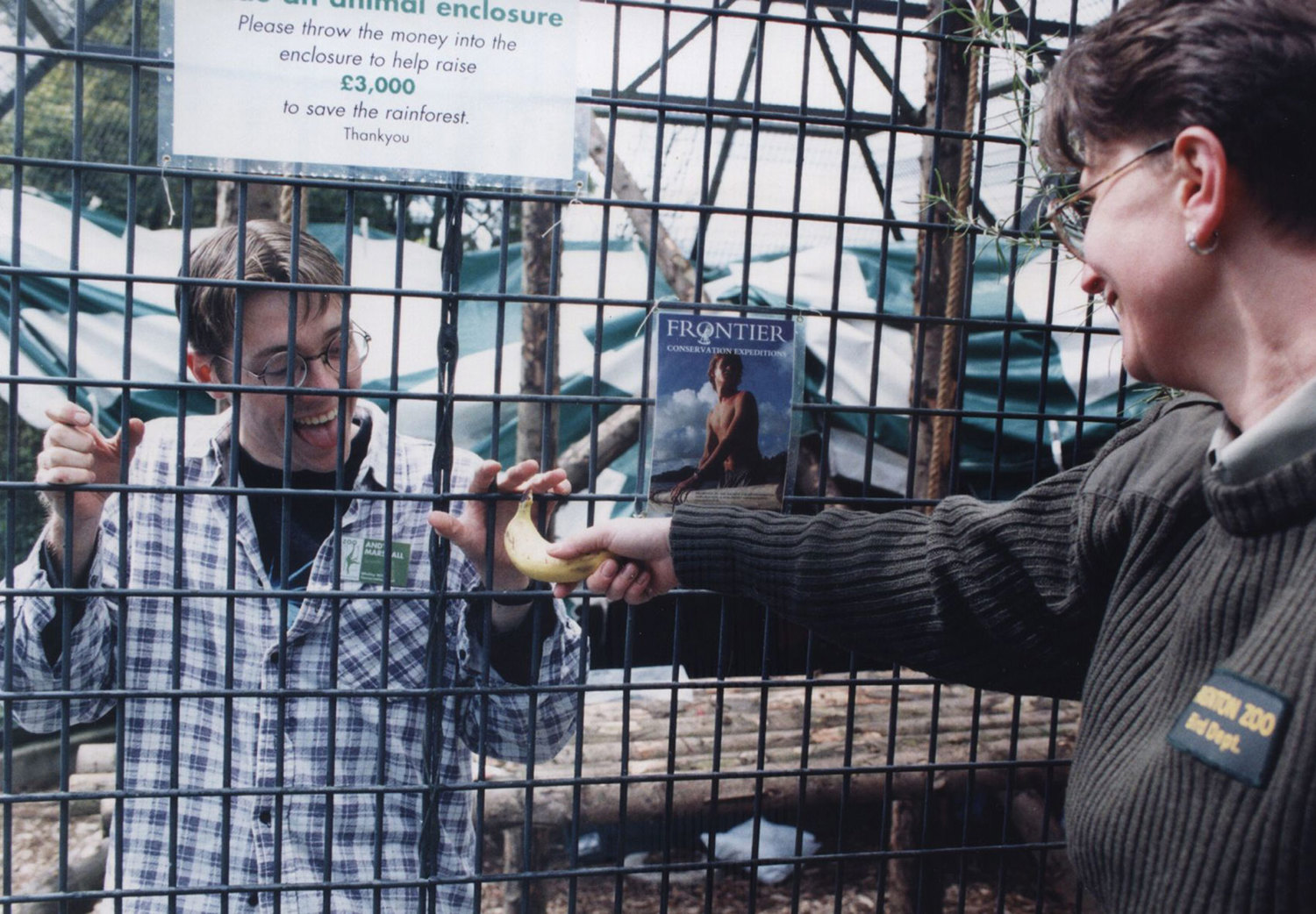 Andy Marshall behind bars in a monkey cage at a zoo handed a banana by the zoo staff.