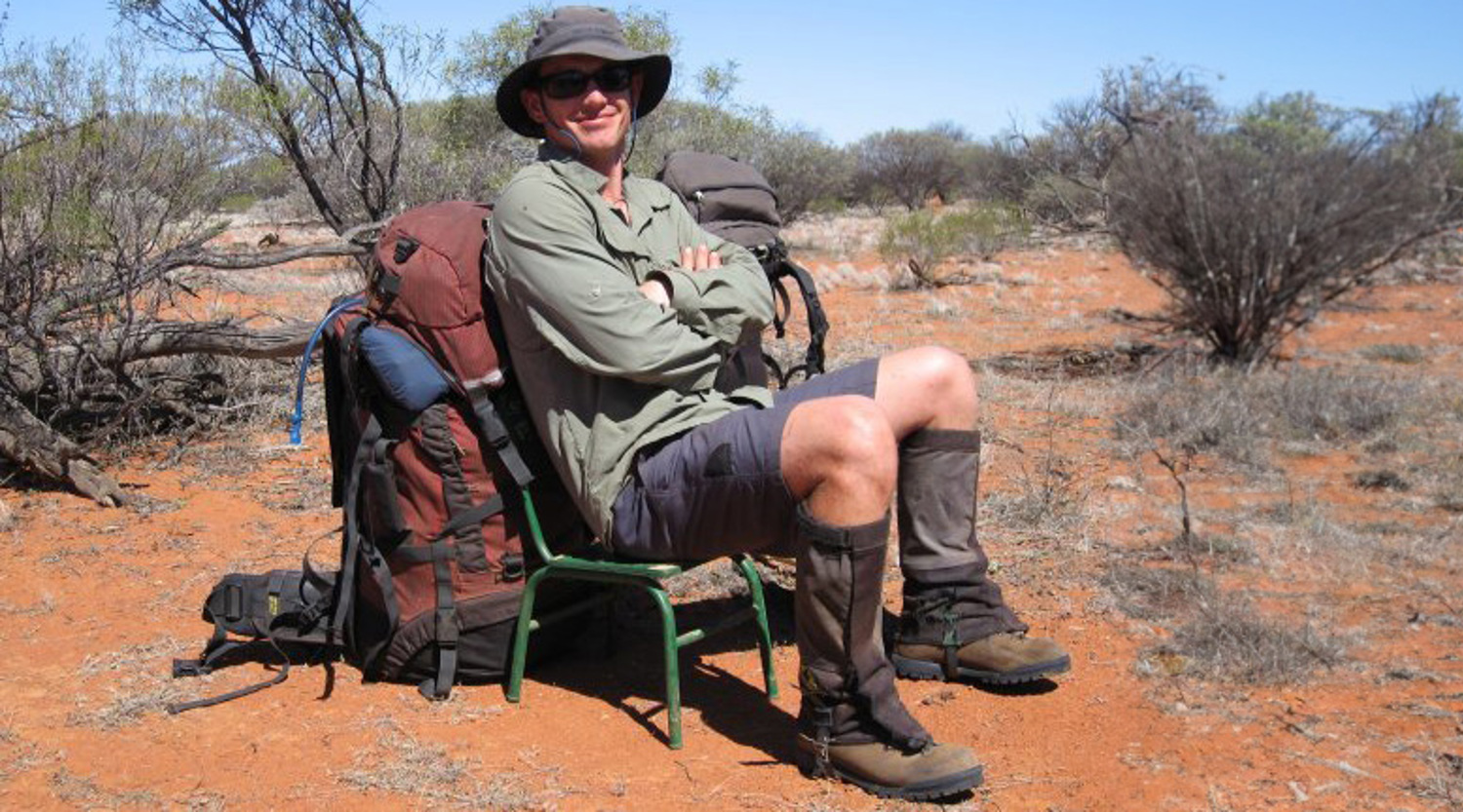 Brendon Munge, dressed in hiking gear, takes a rest on a small green chair leaning against a backpack in the Murchison region of West Australia